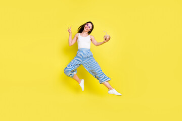 Fototapeta na wymiar Full length body size view of lovely cheerful girl jumping drinking juice showing v-sign isolated over bright yellow color background