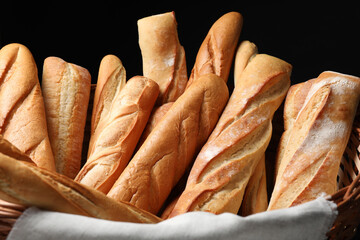 Fresh tasty baguettes in basket against black background, closeup