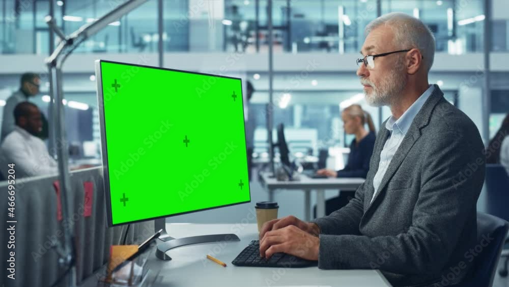 Poster caucasian senior specialist working on desktop computer with green chroma key screen display in a bu