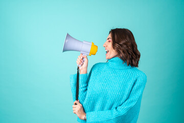 Cozy portrait of a young woman in a knitted blue sweater and bright pink makeup holding a megaphone loudspeaker