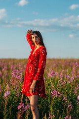 a young beautiful girl, of model appearance, in a beautiful red dress, stands among a red field, freckles on her face, the setting sun illuminates her