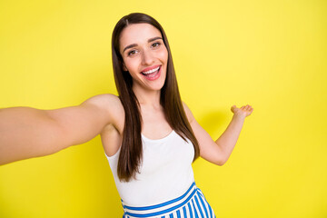 Self-portrait of attractive cheerful girl showing copy space demonstrating new offer isolated over vibrant yellow color background