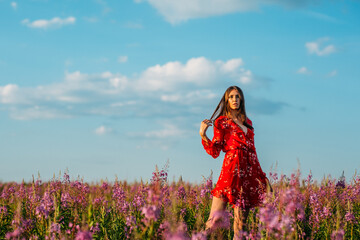 a young beautiful girl, of model appearance, in a beautiful red dress, stands among a red field, freckles on her face, the setting sun illuminates her