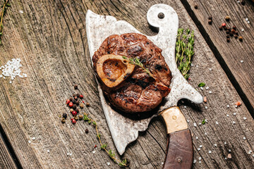 grilled veal shank Osso Buco on metal copper plate on wooden background with meat cleaver on black background. Top view