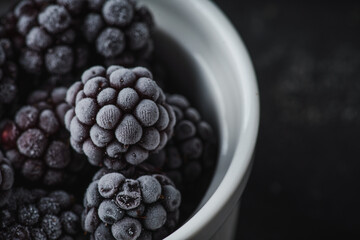 Frozen blackberry in ceramic bowl on rustic wooden background. Selective focus. Shallow depth of field.
