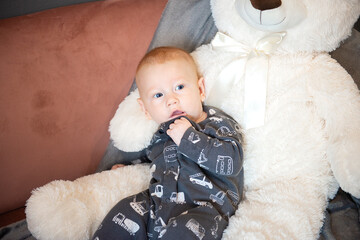thoughtful  newborn baby and big white teddy bear sitting on sofa or couch