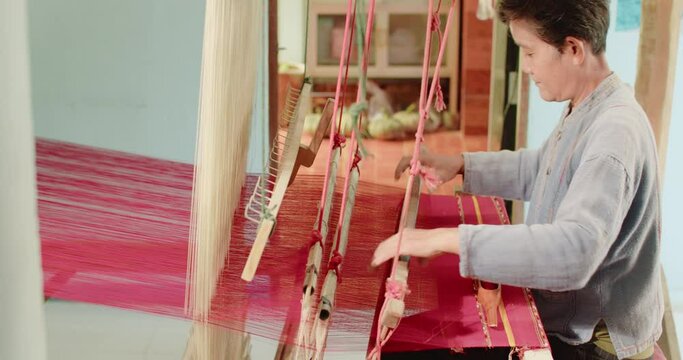 Slow motion scene of an Asian woman weaves Traditional Thai woven cloth for extra income at her home in a rural village of Thailand.