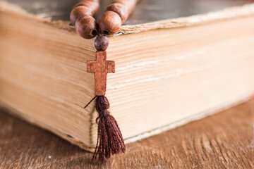 Wooden prayer beads with a Christian cross lie on the holy bible book on a wooden background. The concept of the Catholic and Orthodox faith.