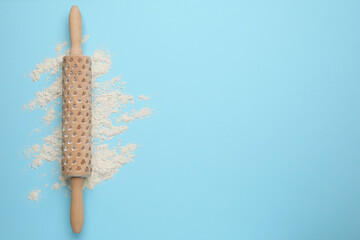 Wooden rolling pin and flour on light blue background, top view. Space for text