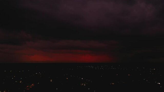 Fly above night city. Red clouds and seldom flash of lightning. Storm in distance. Valladolid, Mexico
