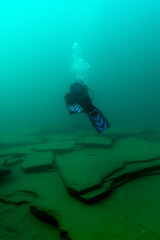 SCUBA diver swimming over large rock plates