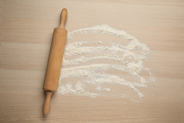Rolling pin and flour on wooden background, top view. Space for text