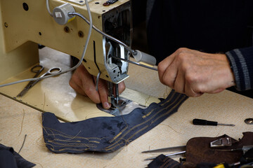 Hands of repairman fixing problems with professional industrial sewing machine in shoemaker workshop. Testing of machine stitching. Selective focus.
