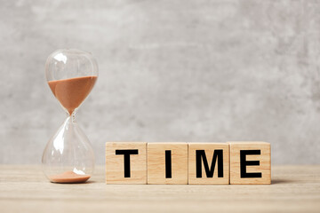 Hourglass with TIME block on table, Sand flowing through the bulb of Sandglass measuring the...