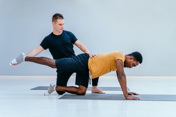 Male pilates trainer helps to african man, individual training participant, do right perform...