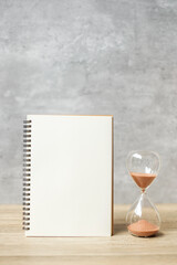 Hourglass with Blank notebook on table, Sand flowing through the bulb of Sandglass measuring the passing. countdown, deadline, Life time and Retirement concept