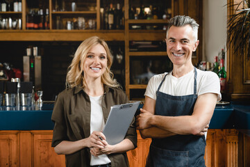 Smiling caucasian small business owner waiter barista with female auditor holding clipboard...