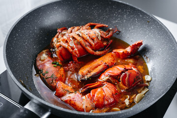 Preparing steaming raw lobster in a deep frying pan. Parts of lobster in pan on stove. Close up. Home cooking. Holidays food