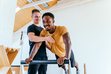 Smiling male coach or instructor help black man client at pilates class in fitness studio. Handsome...
