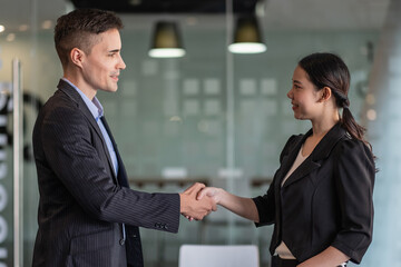 Happy positive business partners finishing meeting. Business man and woman standing in office, shaking hands, smiling, talking. Handshake concept