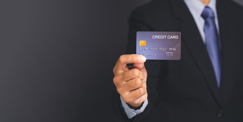 Businessman in a suit holding a mockup blue credit card while standing with a black background in the studio. Close-up photo.  Space for text. Business and finance concept