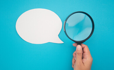 Top view of a blank white speech bubble and hand holding a magnifying glass on a blue background