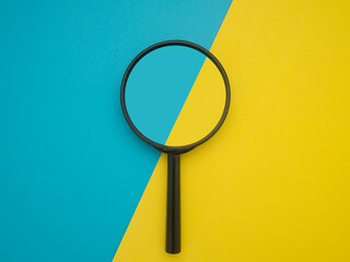 Top view of a magnifying glass isolated on blue and yellow background. Search concept