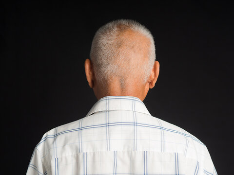 Back view of a senior man in a white shirt standing on black background in the studio. Aged people and healthcare concept