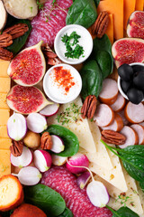 Fototapeta na wymiar Appetizer assortment with sauces on the wooden board. Cheese, salami, olives, figs, radish, spinach, pecan nuts and fried chickpea. Party food