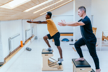 African american man doing exercise on pilates chair equipment. Caucasian male personal trainer...