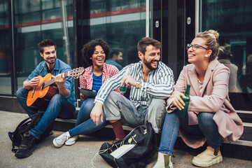 Group of young friends hangout in city.They are sitting,singing and playing guitar.