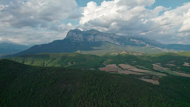 A great mountain, a rock protruding on a plateau in the Pyrenees mountains. Spectacular view of the mountain range from a drone with huge cumulus clouds in the background.