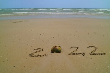 Happy New year 2022 with the waves beat at the beach and shell fragments. Soft focus. Holiday and nature concept.