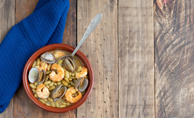 Fabas verdinas with shrimps and clams on a wood background. Copy space.