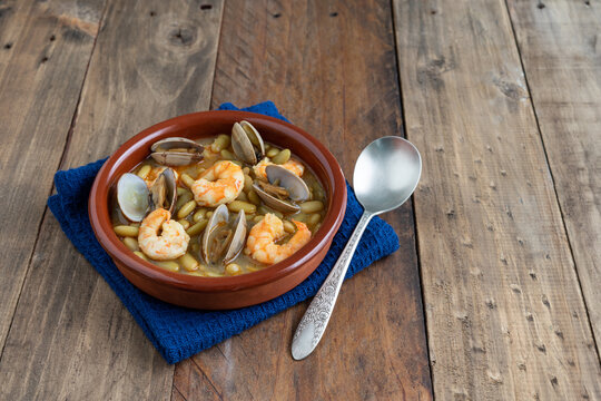 Fabas verdinas with shrimps and clams on a wood background. Copy space.
