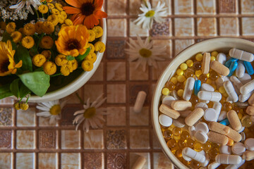 A ceramic bowl with medicinal herbs and a bowl with various pills and tablets are on the countertop. Focus on pills.