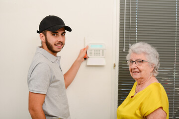handsome young man installing house security anti burglary camera and siren alarm in a senior woman...