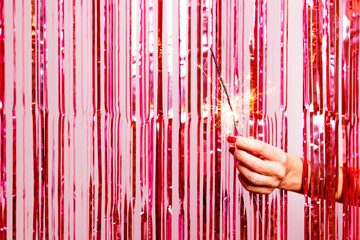 Woman hand  breaking through a pink tinsel with a burning sarkler.