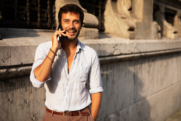 Young stylish man using the phone outdoors. Fashion happy man talking to the phone