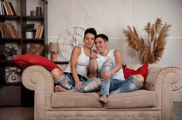 Obraz premium Two girls in love are sitting on the couch and looking at the camera. Watching a movie at home.