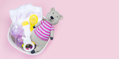 Basket with baby clothes, care cosmetics and toys on pink background with copy space