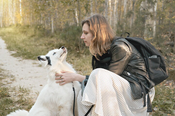 happy yakutian laika dog sitting next to her owner and enjoying love and care. woman stroking and looking at her dog. pet friend, walking with pets in a forest.