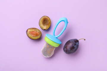 Nibbler with fresh plum on violet background, flat lay. Baby feeder