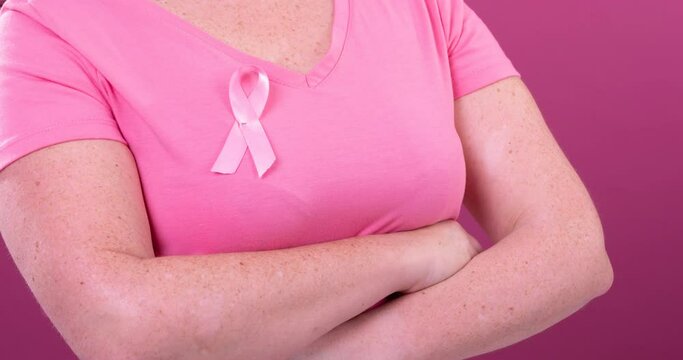 Video of midsection of caucasian woman with crossed arms wearing pink cancer awareness ribbon