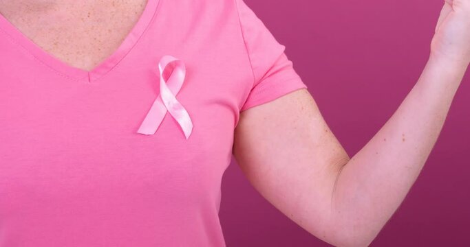 Video of midsection of caucasian woman wearing pink cancer awareness ribbon, with pink background