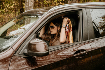 A young beautiful girl in a headscarf is sitting in an expensive brown car.