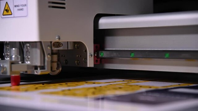 An industrial advertising plotter close-up cuts a template on the cardboard packaging for products. shallow depth of field in real time. Live camera