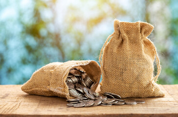 Bags filled with coins on wooden table with sunlight, blurred background