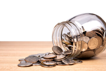 Coins spilling from a money jar on table with white background.