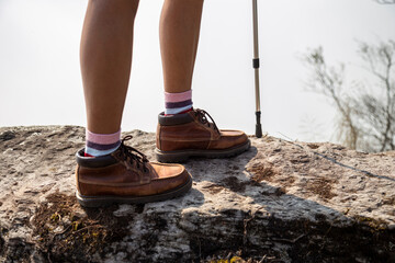 Hiking woman wearing trekking boots standing on the rock of mountain.